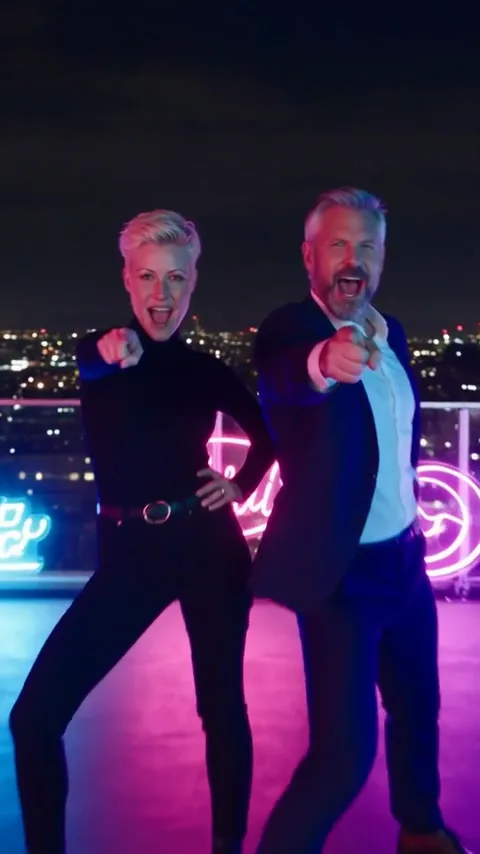 Les deux personnages en train de chanter et danser sur un toit éclairé au néon la nuit